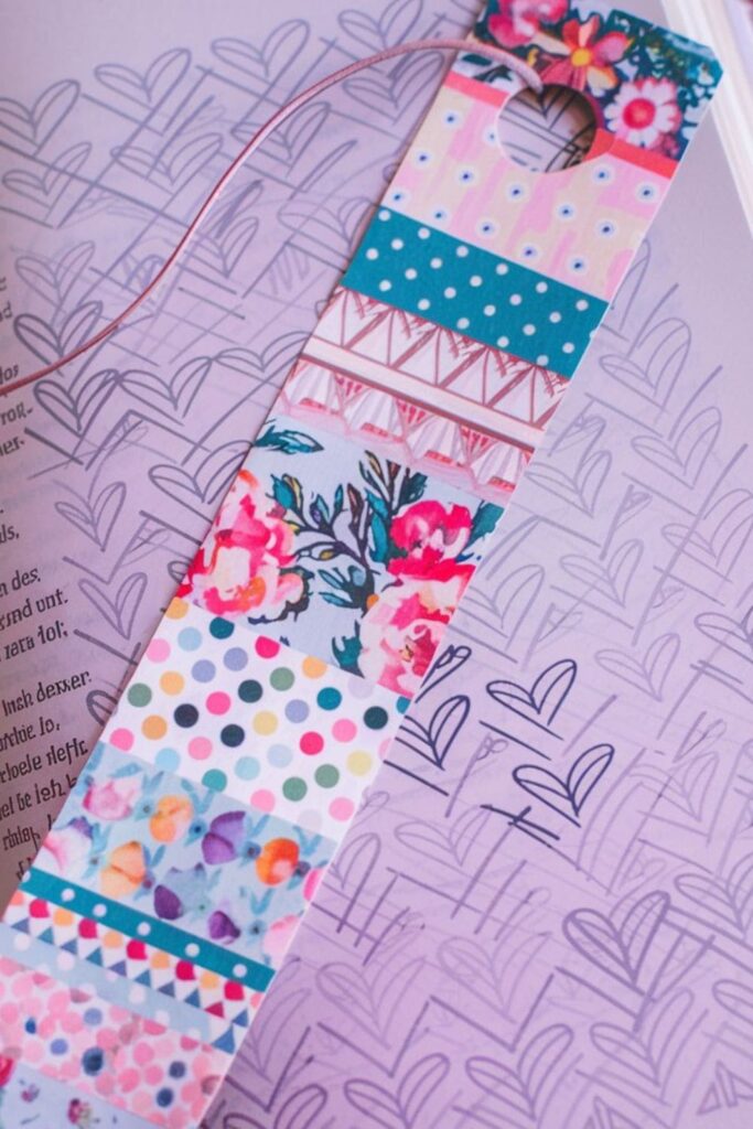 A DIY bookmark layered with colorful washi tape in various patterns such as floral, geometric, and polka dots, finished with a punched hole and ribbon
