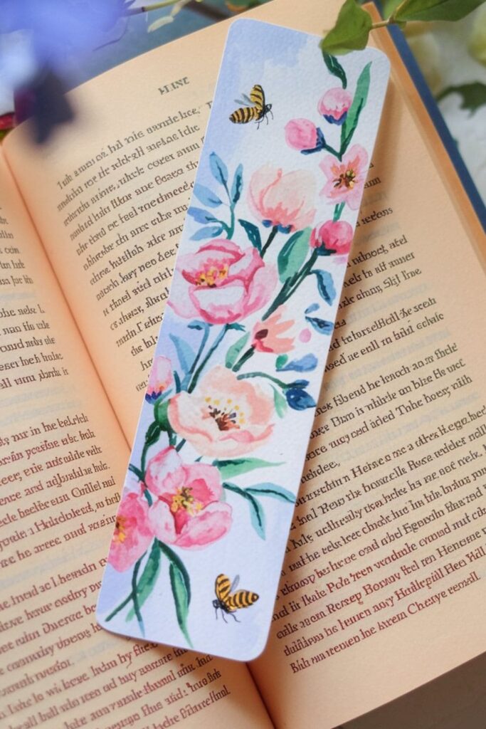 A floral-themed bookmark with hand-painted cherry blossoms, pastel pink and green hues, and small illustrations of butterflies and bees for a fresh springtime feel