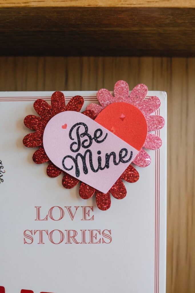 A heart-shaped bookmark made of red and pink felt or cardstock, designed with a small slit in the middle to securely slide onto a book page